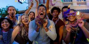 A group of friends in their twenties smiling and laughing at the camera, wearing lots of Mardi Gras beads
