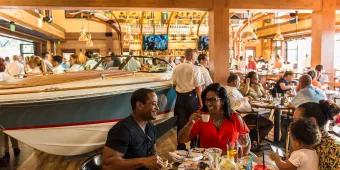 The Boathouse People eating in a full restaurant dining room sat at tables surrounding a large speedboat