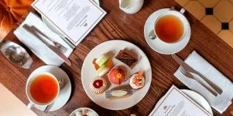 A birds eye view of a table with two cups of tea, a plate of cakes and an afternoon tea menu