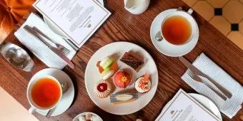 Mother's Day Afternoon Tea A birds eye view of a table with two cups of tea, a plate of cakes and an afternoon tea menu