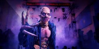 Halloween Horror Nights 2023 A bald man with tentacle-like features covering his mouth and long pointed fingernails leaning in to the camera