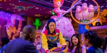 A server bringing a basket full of food to a table of 2 adults and 2 children. There is Toy Story theming in the background including a figure of Bo Peep
