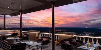 A terrace with sofas, tables and chairs looking out over a purple and pink toned sunset