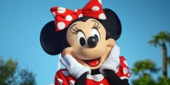 Minnie Mouse in a red polka dot dress with her hands held up to her cheeks in front of a blue sky