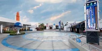 A paved plaza surrounded by space themed buildings, with a large model of the NASA logo to the left-hand side