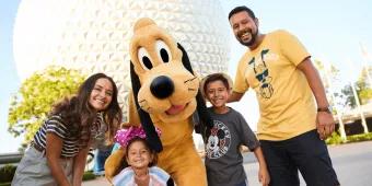 A mother and father with a young boy and young girl posing with Pluto in front of Spaceship Earth