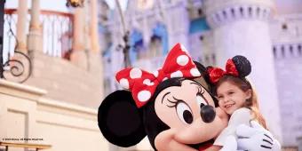 A young girl wearing a blue Magic Band hugging Minnie Mouse in front of Cinderella Castle at Walt Disney World