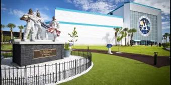 Apollo V Center at Kennedy Space Center A statue of three astronauts holding an American flag in front of a building with a large sign reading Apollo NASA