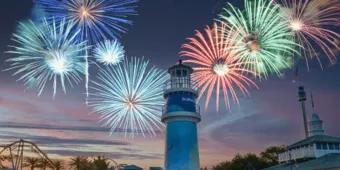 Multi-coloured fireworks being set off above a lighthouse as the sun is setting