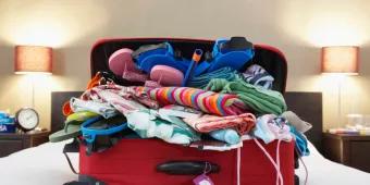 A red suitcase on top of a bed overflowing with clothes 