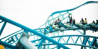 People riding a coaster with ride vehicles shaped like snowmobiles on a blue track