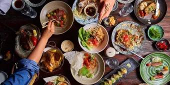 A table full of plates of food with people reaching over to take food with chopsticks