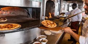 A chef taking a pizza out of a wood fired pizza oven at California Grill