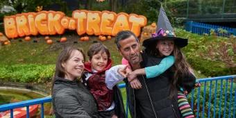 A family posing in front of a sign reading "Brick or Treat". The two children are dressed in Halloween costumes