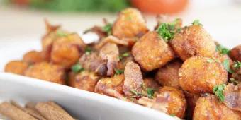A bowl of sweet potato tots topped with bacon and herbs