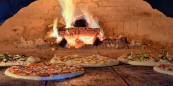 5 pizzas cooking in a large wood-fired pizza oven