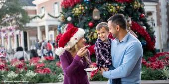 A man holding a small boy who is smiling at a woman eating a cookie and wearing a Santa hat