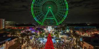 A view over ICON Park with a red Christmas tree in the foreground and The Wheel lit up green in the background