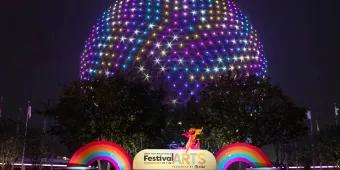 Spaceship Earth lit up in rainbow colours behind a sign reading Festival of the Arts