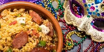A dish of jambalaya on a table next to a sequined mask and multicoloured beads