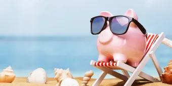 A pink piggy bank wearing sunglasses and sitting on a deck chair on a beach