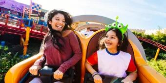 A woman smiling at a young girl on the Slinky Dog Dash ride, the girl has a headband on with a green alien head, three eyes and an antenna.