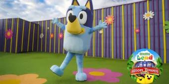 Big blue dog called Bluey with arms extended open and the Alton Towers CBeebies Land logo in the bottom right corner