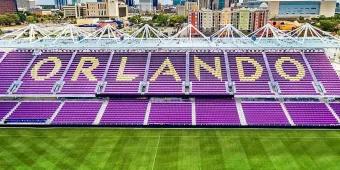 One side of a football stadium's seats with a cityscape in the background. The seats are purple with detailing that spells out "Orlando"