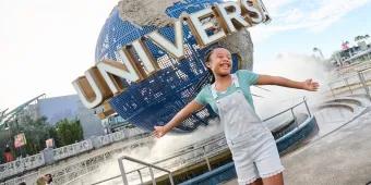 A girl standing with her arms outstretched in front of the Universal Studios globe