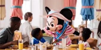 Minnie Mouse greeting two young children and their dad while they are sat round a table eating breakfast