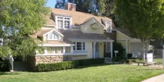 Universal's Studio Tour Cream coloured suburban style home with green lawn in the front and a large tree to the left. There is an American style post box outside as well.