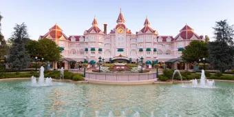 The exterior of a pink hotel behind a fountain and a flower bed in the shape of Mickey Mouse