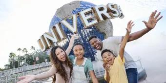A family of four stood in front of a big circular statue of the globe with white capital letters on spelling UNIVERSAL. The family are smiling and have their arms spread wide. There is a couple with one daughter and one son.