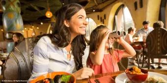 Dining at Walt Disney World Resort A mum and young girl sat at a table eating dinner. The girl is using binoculars to look out the window