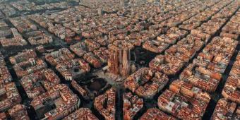Barcelona Layout of Barcelona with a view of the Sagrada Familia cathedral. The city is laid out with straight roads and buildings shaped in squares. They all have the same colour scheme with white and orange walls and roofs.