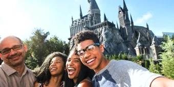 Hogwarts Castle Selfie of family of four stood on bridge in front of the Hogwarts Castle. There is a boy holding the camera, besides him is a young woman, an older woman and an older man. All are smiling with joy.