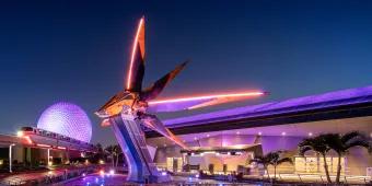 EPCOT EPCOT, the guardians of a galaxy triangular space ship coloured yellow and grey. In the background there is a white golf ball shaped building and the monorail.