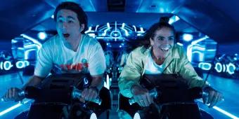 TRON Lightcycle/Run at Magic Kingdom Park Two young adults sat on motorcycles shaped vehicles TRON Lightcycle. They are leaning forward gasping with shock.