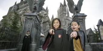 The Wizarding World of Harry Potter Two young girls wearing wizard robes and pointing magic wands at the camera while standing in front of Hogwarts Castle