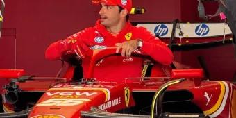 Carlos Sainz in Ferrari Famous Ferrari driver hopping in his famous Formula 1 Ferrari car in the garage with red walls. He is wearing a red cap which is branded and is wearing a red hoodie with the Ferrari logo on it.