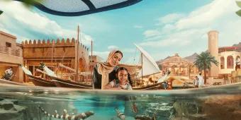 SeaWorld Abu Dhabi Mum and daughter stood looking into clear water with many different fish swimming around. In the background there are stone buildings and wooden boats.