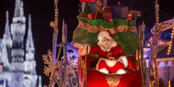 Santa Claus in Magic Kingdom Park Santa Claus sat on a sleigh on a float full of presents. In the background Cinderella Castle is lit in white colours.