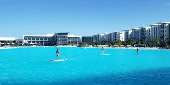 Evermore Resort Huge white building (hotel) and smaller villas surrounding a huge crystal clear pool which looks so big it could be a lake. People are paddleboarding on it.