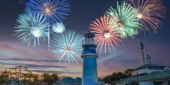 SeaWorld Orlando The iconic blue lighthouse at the front of the park with fireworks of many different colours exploding in the background above the silhouette of a ride,