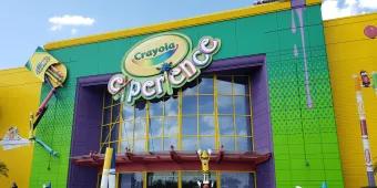 Crayola Experience Large modern building coloured yellow, green and purple has big sign saying Crayola Experience on it. There are giant crayons outside with faces on them.