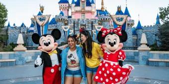 Disneyland Park Two young women stood with Mickey and Minnie in front of a pink and blue castle.
