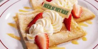 Butterbier™ Crepes Zwei geviertelte Crêpes mit Schlagsahne, gelber Soße und Erdbeerscheiben.