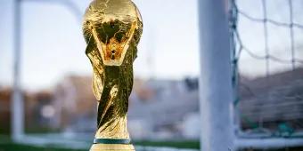 FIFA 2026 World Cup A gold trophy with a globe at the top and things wrapping around it sat in front of a white football goal.