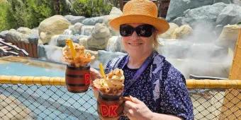 Bubbly Barrel’s DK Crush Float with Mug Woman in theme park holding two barrel themed mugs filled with drinks, whipped cream, sprinkles and more.
