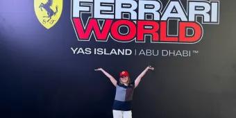 Girl stood in front of Ferrari World sign which has black background, red and white text and the Ferrari logo next to the name.